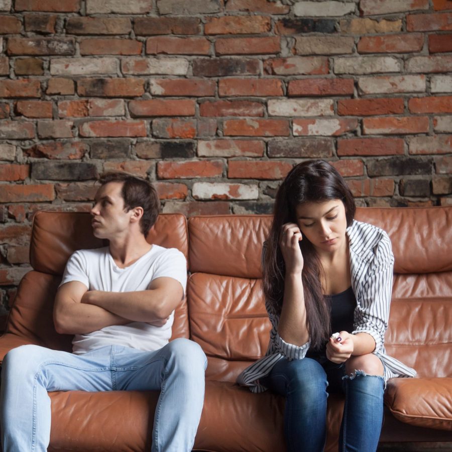 Frustrated upset couple in quarrel not talking after fight, offended stubborn insulted jealous man sitting silent on sofa at home with sad depressed disappointed woman, marriage relationships problem