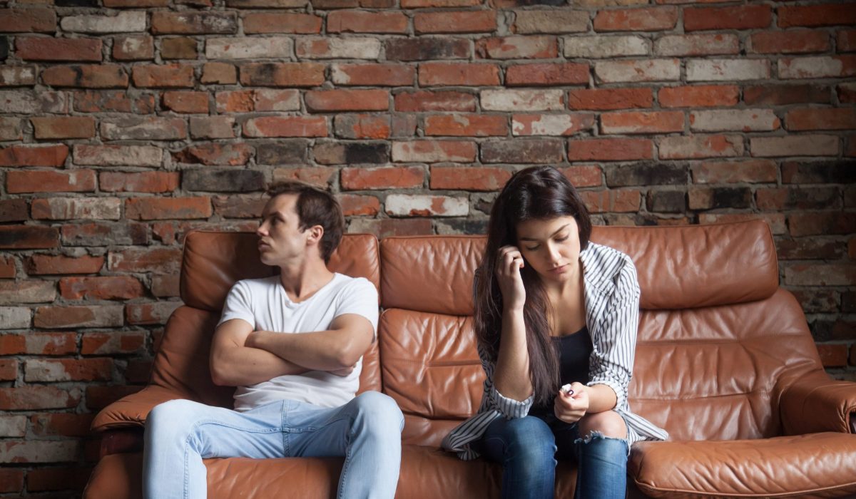 Frustrated upset couple in quarrel not talking after fight, offended stubborn insulted jealous man sitting silent on sofa at home with sad depressed disappointed woman, marriage relationships problem